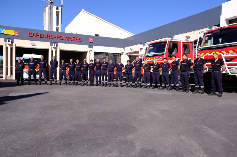Sapeurs-pompiers rassemblés devant la caserne et les véhicules d'intervention